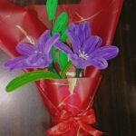 Handmade purple flower bouquet wrapped in red paper with a satin ribbon.