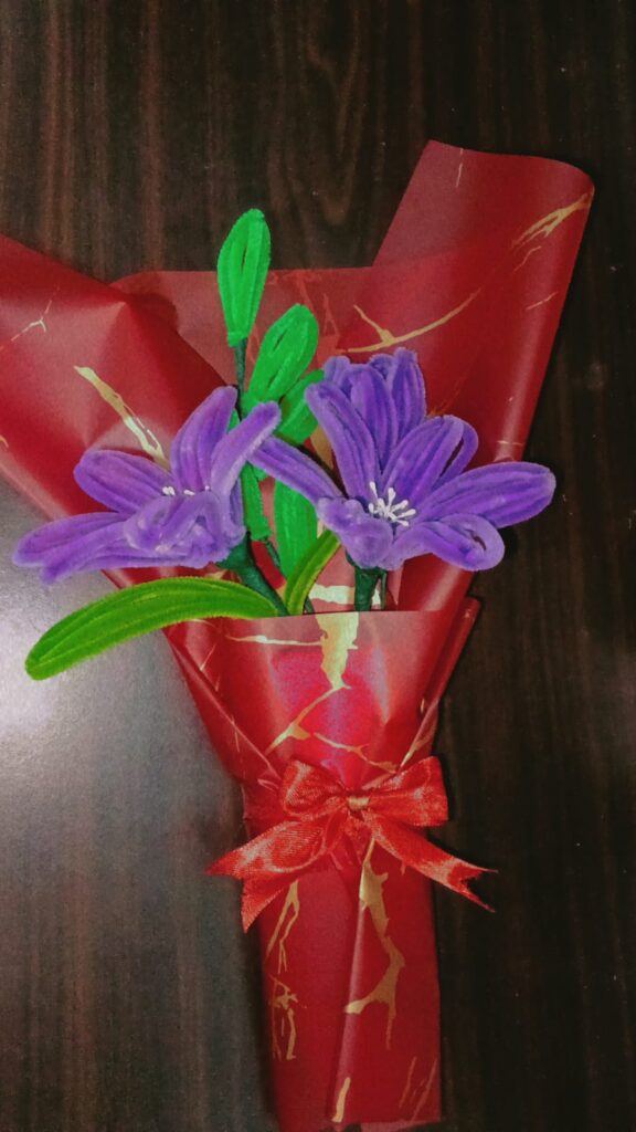 Handmade purple flower bouquet wrapped in red paper with a satin ribbon.
